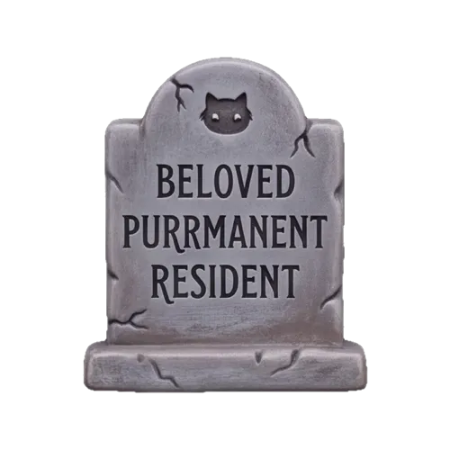 A gray tombstone carved with a cat face and the words Beloved Purrmanent Resident